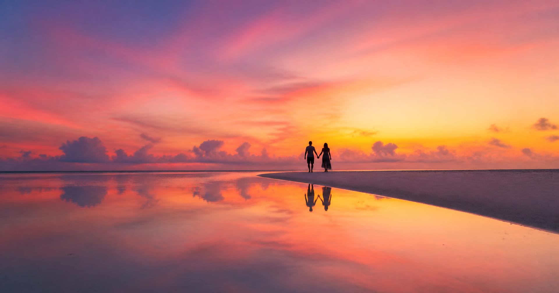 Couple walking along a Maldives sandbank at sunset